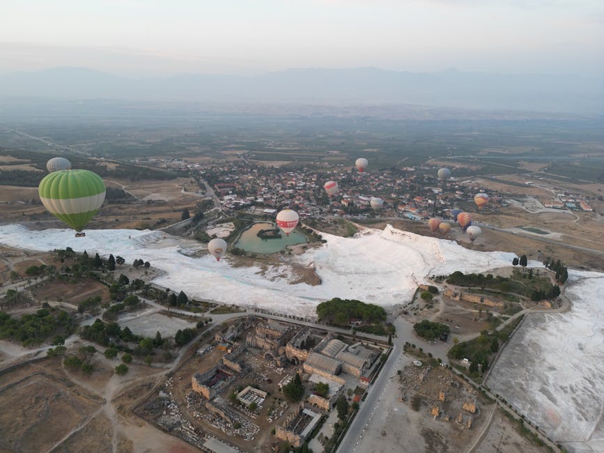 Stunning aerial shot of Pamukkale, Türkiye, dotted with colorful hot air balloons at sunrise.