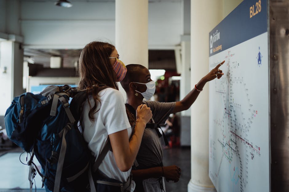 Two masked travelers checking a subway map to find their direction indoors.
