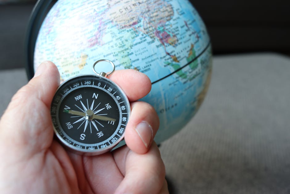 A hand holding a compass in front of a globe, symbolizing travel and navigation.