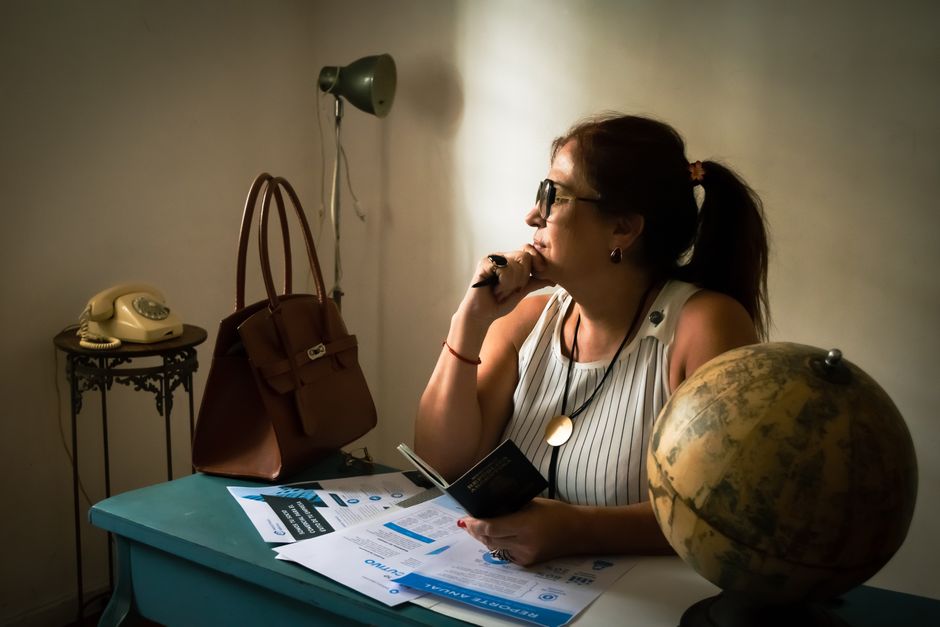 A woman in a vintage office contemplating with a globe, documents, and classic phone.
